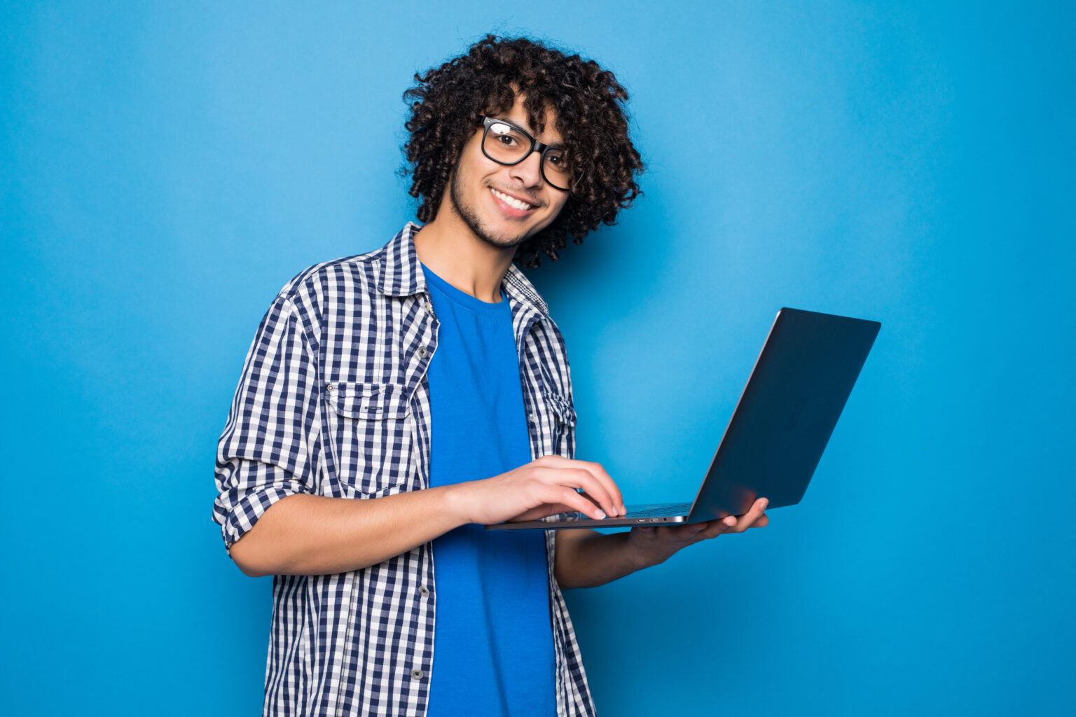 Young curly man with laptop isolated on blue background